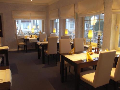 un restaurante con mesas, sillas blancas y ventanas en Hohwachter Hof, en Hohwacht