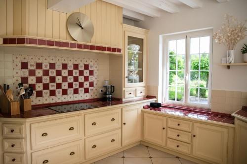 une cuisine avec des placards blancs et une horloge murale dans l'établissement Villa des Saules, à Le Bec-Thomas