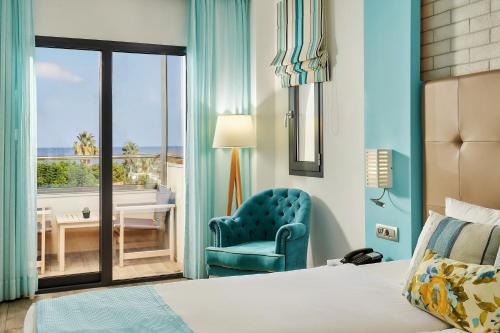 a bedroom with a bed and a chair and a window at Sentido Kyknos Beach Adults Only in Malia