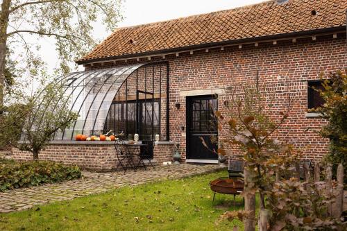 a brick house with a greenhouse in a yard at Het Ovenhuisje in Denderwindeke