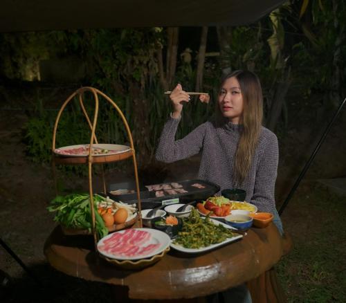 a woman sitting at a table with a plate of food at ปางสูงเฮาส์ pangsung house บ้านมินิ เหลือง in Ban Pang Bo Hu Bon