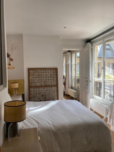 a white bedroom with a large bed and windows at Appartement à deux pas du canal Saint Martin in Paris