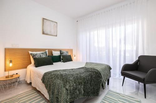 a white bedroom with a bed and a chair at Parque dos Reis Apartment 4 A in Monte Gordo