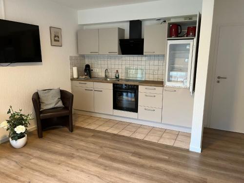 a kitchen with white cabinets and a tv and a chair at Appartement Gartenglück in Nordhorn