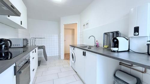 a white kitchen with a sink and a counter at Neumünster Apartments direkt an der Stadthalle mit WLAN & Parkplatz in Neumünster