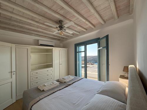 a white bedroom with a bed and a window at Almyra Yellow Villa in Kithnos