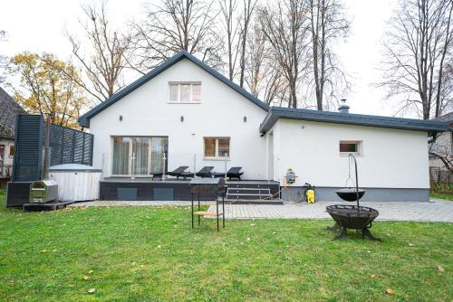 a white house with a grill in the yard at Luxury Guest House - Hot Tub & Sauna in Valmiera