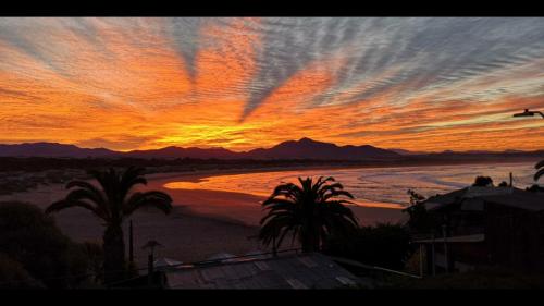 a sunset over a beach with palm trees and the ocean at Casa Mirador in Quintero