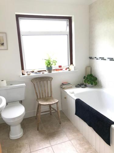 a bathroom with a toilet and a tub and a chair at Rowantree in Kiltarlty