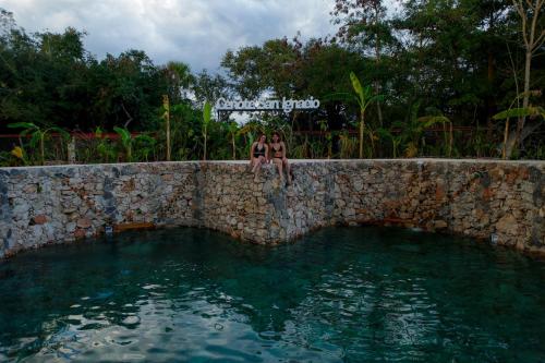 two men sitting on a stone wall next to a swimming pool at Hacienda Cenote San Ignacio in Chocholá