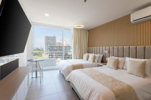 two beds in a hotel room with a large window at Aparta suite Playa Bello Horizonte Santa Marta in Santa Marta
