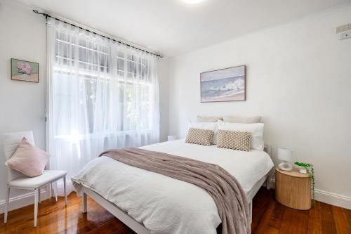 a white bedroom with a bed and a window at Orton Blue- Beachside getaway for 4, Pets welcome, Aircon, Park and walk to everything! in Ocean Grove