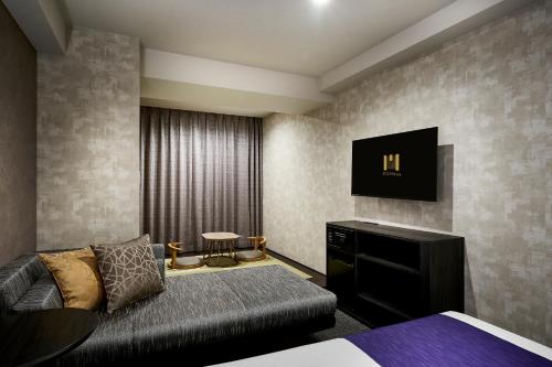 a bedroom with a couch and a tv on the wall at hotel MONday KYOTO MARUTAMACHI in Kyoto