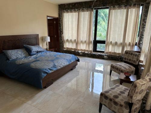 a bedroom with a bed and a chair and windows at Villa Vambú, Chiriquí, Panamá in Chiriquí
