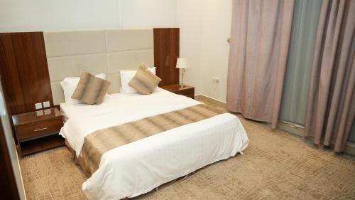 a hotel room with a bed with white sheets and pillows at هذه ليلتي- اليرموك- طريق الدمام This Lailaty Al Yarmouk-Dammam Road in Riyadh