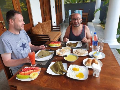 twee mannen aan een tafel met ontbijt bij Summer Heritage Villa in Unawatuna