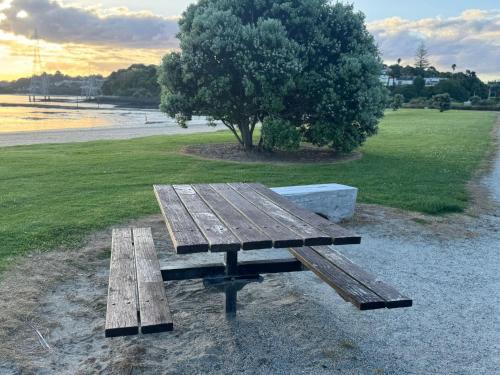 a wooden bench sitting next to a field with a tree at Auckland City cozy Stay in Auckland