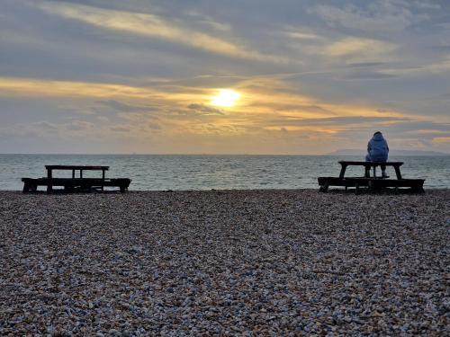 a person sitting on a bench on the beach at Seaside Holiday Home Inside a Resort in Selsey