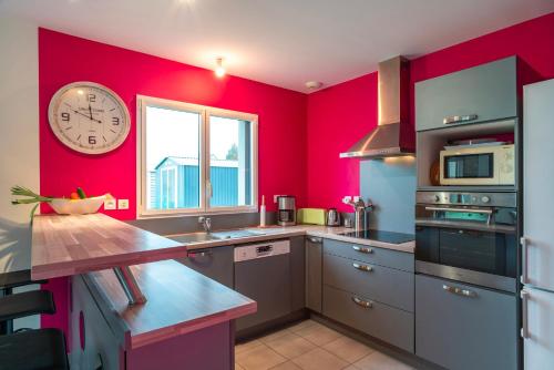 une cuisine avec des murs rouges et une horloge murale dans l'établissement La Villa de l'Odet - 4 Chambres et parking privé, à Pleuven
