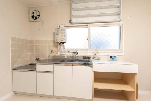 a white kitchen with a sink and a window at アンドステイ西戸部町2丁目 in Nishi-hiranumachō