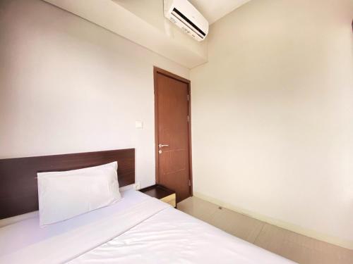 a bedroom with a white bed and a brown door at Fancy 2BR at Skyland City Jatinangor Apartment By Travelio in Sumedang