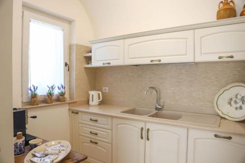 una cucina con mobili bianchi, un lavandino e una finestra di Country Trullo Rosso With Jacuzzi Alberobello a Locorotondo