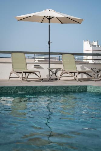 two chairs and an umbrella next to a swimming pool at BYPILLOW La Sal in Cádiz