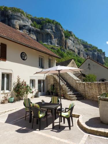 a table with chairs and an umbrella in front of a building at Votre gîte au Domaine du Lynx in Baume-les-Messieurs