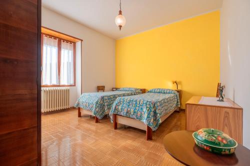 two beds in a room with yellow walls and a table at Appartamento Casa Rita - Sorano in San Giovanni delle Contee