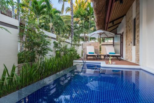 an outdoor swimming pool with two chairs and an umbrella at Henann Resort Alona Beach in Panglao
