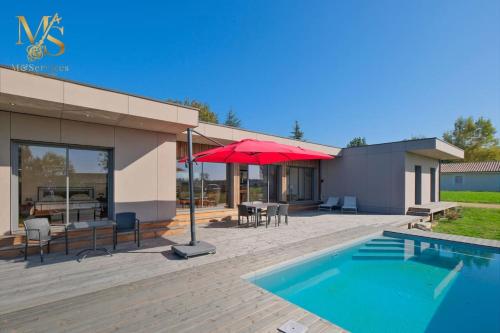 une terrasse avec une piscine et un parasol rouge dans l'établissement Maison Moderne avec Piscine au Cœur des Vignes, à Bergerac