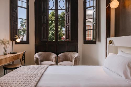 a bedroom with a bed and two chairs and windows at MASANET Emblematic Hotels - Adults Only in Las Palmas de Gran Canaria