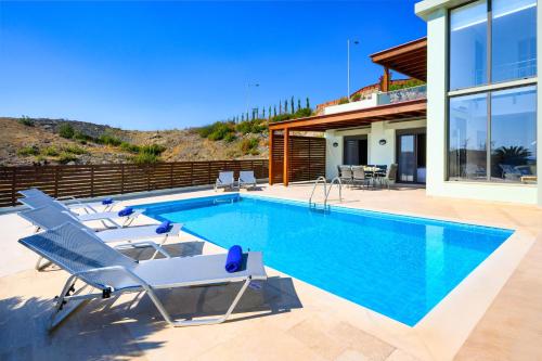 a swimming pool with lounge chairs and a house at Gonos Villas in Asklipiḯon
