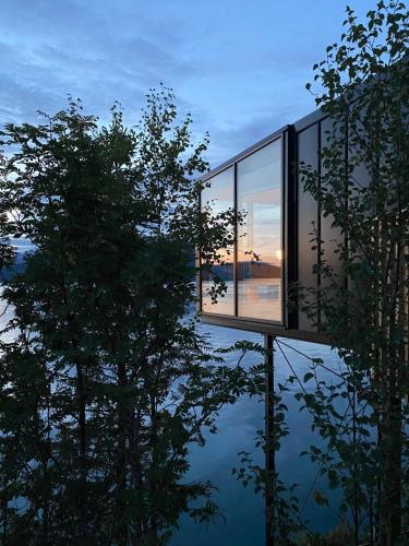 a glass house with a tree reflection in the water at Yttervik in Mo i Rana