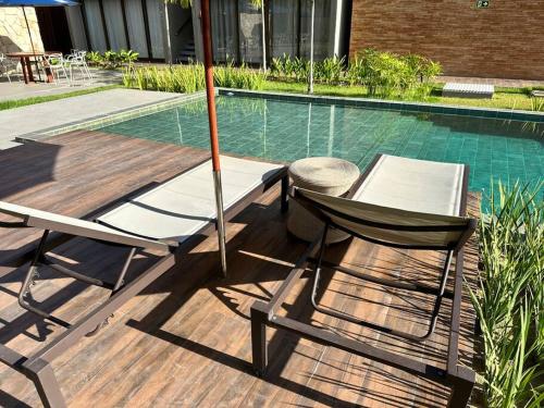 two chairs and an umbrella next to a swimming pool at Villa Naluri - Studio A001 no paraíso Japaratinga! in Japaratinga