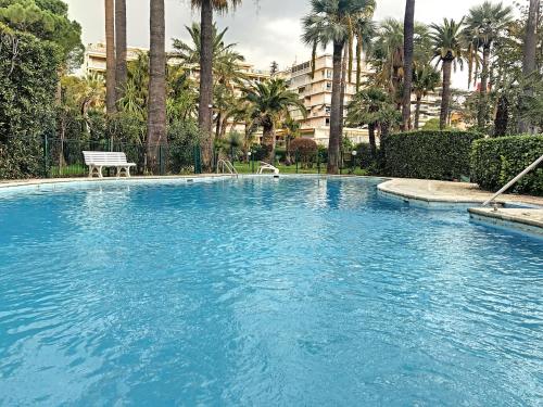 une grande piscine bleue avec un banc et des palmiers dans l'établissement A 2 pas des plages piscine 183L STENJ, à Cannes