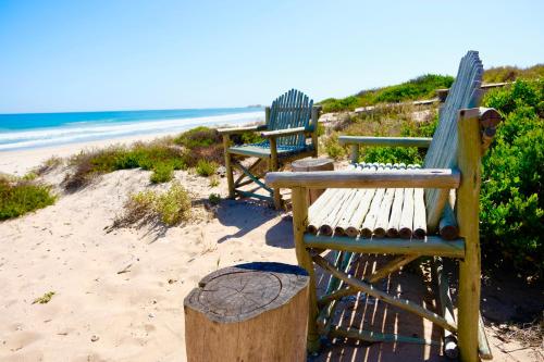two wooden benches sitting on the sand at the beach at Sea Lily Holiday Home - Your Coastal Sanctuary! in Stompneusbaai