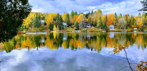 a lake with houses and trees reflecting on the water at Entre Monts et Lac - lac - Lake front & Volleyball in Saint Adolphe D'Howard