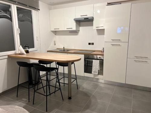 - une cuisine avec des placards blancs, une table en bois et des tabourets dans l'établissement Le Marceau, appartement proche centre ville, à Besançon