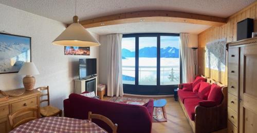 Elle comprend un salon doté d'un mobilier rouge et d'une grande fenêtre. dans l'établissement Appartement avec vue exceptionnelle au pied des pistes, à L'Alpe-d'Huez