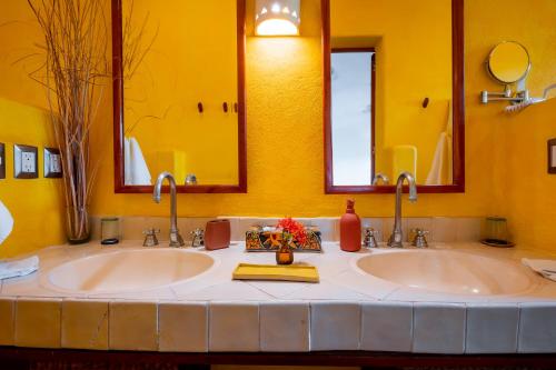 two sinks in a yellow bathroom with two mirrors at Ensueño de Fuga in Zihuatanejo