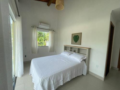 a white bedroom with a bed and a window at Casa Ipoméia Azul in Itacaré