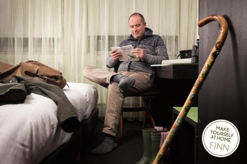 a man sitting on a bed holding a remote control at Hotel Finn in Almere