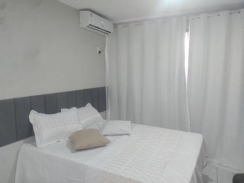 a white bed with white pillows and a window at Apto 352 centro nucleo bandeirant in Brasilia