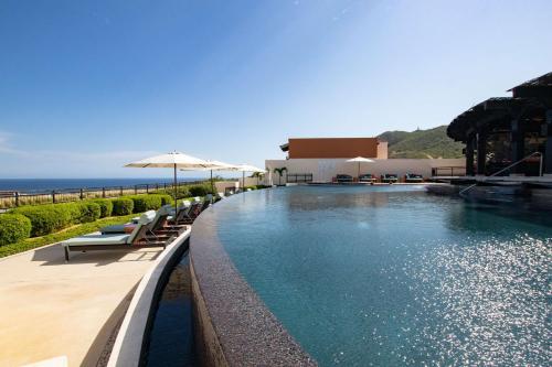 a pool with chairs and umbrellas next to the ocean at Cabo Cottage Copala · Stunning * Luxury Ocean View 2BR*Resort Living in Cabo San Lucas
