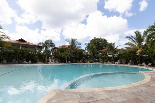 a large swimming pool in a resort with palm trees at Coastal Luxury 2-Bed w Pool Access in Bayahibe in Bayahibe