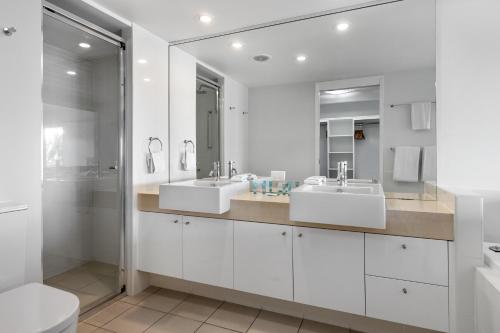 a white bathroom with two sinks and a shower at Beaches on Lammermoor Apartments in Yeppoon