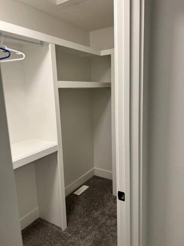 an empty closet with white shelves in a room at The Happy place - Luxurious, Cozy and Modern Home with Air-condition, Netflix, Free Parking close to Airport and West Edmonton Mall in Edmonton
