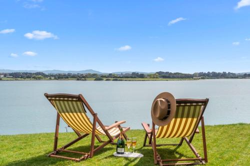 two chairs sitting on the grass next to a lake at Black Hut Eco Retreat in Christchurch