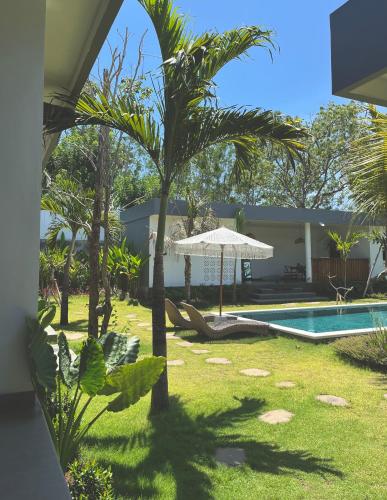 a yard with a pool and a palm tree and an umbrella at Tropical Almond Villa in Uluwatu